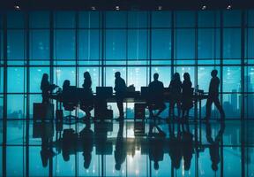 Silhouettes of employees collaborating at a large desk with office equipment photo
