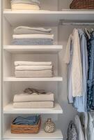 Minimalist closet with clean white shelves, neatly organized clothes, and a few decorative elements photo