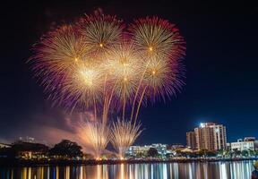 Bright fireworks exploding in the night sky over a cityscape, reflecting off nearby buildings and water photo