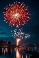 Bright fireworks exploding in the night sky over a cityscape, reflecting off nearby buildings and water photo