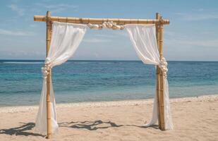 A bamboo arch with white drapes on the beach photo