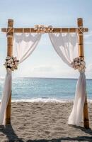 A bamboo arch with white drapes and shells on the beach photo