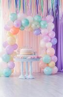 A colorful birthday setup with pastel balloons, a large cake table, and streamers hanging from the ceiling, creating a festive atmosphere photo