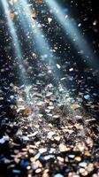 A shower of glittering confetti, highlighted by piercing light rays that create sharp contrasts between the bright pieces and the dark background photo
