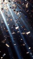 A cascade of metallic confetti falling in slow motion, with radiant beams of light piercing through the darkness, highlighting each piece in vivid detail photo