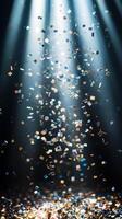 A shower of glittering confetti, highlighted by piercing light rays that create sharp contrasts between the bright pieces and the dark background photo