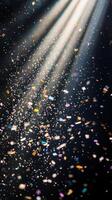 A shower of glittering confetti, highlighted by piercing light rays that create sharp contrasts between the bright pieces and the dark background photo