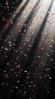 Abstract image of falling confetti illuminated by soft, scattered light rays, creating a magical and ethereal atmosphere over a black background photo