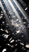 Dynamic image of swirling confetti, caught in beams of white light, with the dark background enhancing the brightness and movement of the scene photo
