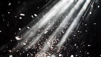 Dynamic image of swirling confetti, caught in beams of white light, with the dark background enhancing the brightness and movement of the scene photo