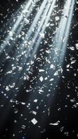 Dynamic image of swirling confetti, caught in beams of white light, with the dark background enhancing the brightness and movement of the scene photo