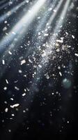 Dynamic image of swirling confetti, caught in beams of white light, with the dark background enhancing the brightness and movement of the scene photo