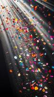 Multicolored confetti raining down against a black backdrop, with dramatic light rays streaming through the scene, casting shadows and reflections photo