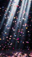 Soft, multicolored confetti drifting through shafts of light, with the dark background creating a stark, captivating contrast photo