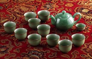 A green tea set on a red and gold patterned rug photo