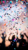A close-up of falling confetti in focus, with blurred silhouettes of people celebrating in the background photo