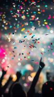 A close-up of falling confetti in focus, with blurred silhouettes of people celebrating in the background photo