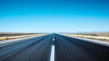 A wide-angle shot of an empty highway stretching into the horizon under a clear blue sky photo