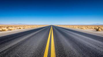 A wide-angle shot of an empty highway stretching into the horizon under a clear blue sky photo