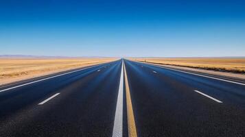 A wide-angle shot of an empty highway stretching into the horizon under a clear blue sky photo