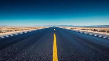 A wide-angle shot of an empty highway stretching into the horizon under a clear blue sky photo