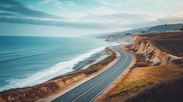 Empty coastal highway hugging the shoreline, with the ocean to one side and cliffs on the other photo