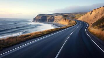 Empty coastal highway hugging the shoreline, with the ocean to one side and cliffs on the other photo
