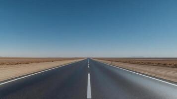 A wide-angle shot of an empty highway stretching into the horizon under a clear blue sky photo