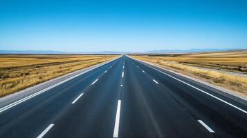 A wide-angle shot of an empty highway stretching into the horizon under a clear blue sky photo