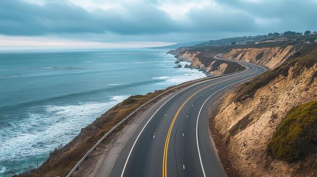 Empty coastal highway hugging the shoreline, with the ocean to one side and cliffs on the other photo