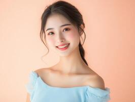 Beauty portrait of a young Asian woman in a sky-blue dress, softly smiling against a pastel peach background with room for copy photo