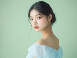 Beauty portrait of a young Asian woman in a powder blue dress, her hair tucked behind her ears, against a pastel green background with copy space photo