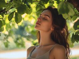 Relaxed woman standing under a tree, eyes closed, feeling the cool breeze, surrounded by nature with ample copy space in the background photo