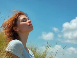 Woman on the edge of a grassy hill, eyes closed, enjoying the calmness of the open space, with wide copy space provided by the blue sky photo