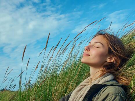 Woman on the edge of a grassy hill, eyes closed, enjoying the calmness of the open space, with wide copy space provided by the blue sky photo