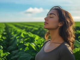 A woman outdoors, standing in a lush green field, eyes closed, breathing deeply, with plenty of blue sky in the background for copy space photo