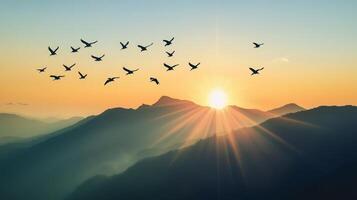 A flock of birds flying over a mountain range, silhouetted against the rising sun photo