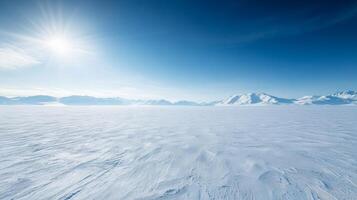 A wide, snow-covered plain stretching into the horizon, with distant mountains under a bright, cloudless winter sky photo
