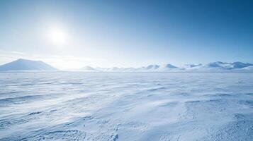A wide, snow-covered plain stretching into the horizon, with distant mountains under a bright, cloudless winter sky photo