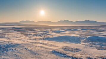 A vast, open tundra under a pale winter sun, with snowdrifts and distant mountain ranges in the background photo