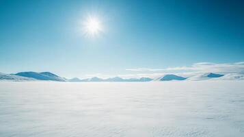 A wide, snow-covered plain stretching into the horizon, with distant mountains under a bright, cloudless winter sky photo