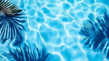 Bright blue pool water with gentle waves and bold tropical leaves' shadows cast across the surface photo
