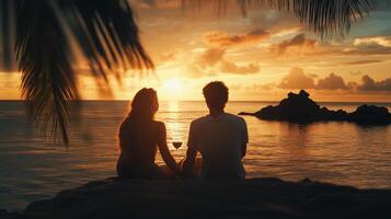 A couple enjoying a sunset by the ocean during their vacation on a tropical island photo