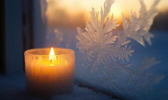 A candle is lit in front of a window with snowflakes on the glass photo