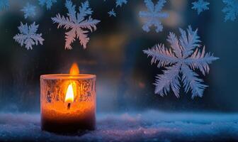 A candle is lit in front of a window with snowflakes falling outside photo
