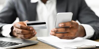 A person holds a credit card in their left hand and a smartphone in their right hand while looking at the screen. photo