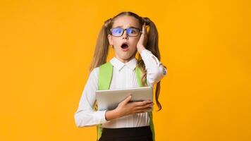 Oops, Gadget Problem. Confused Schoolgirl Clutching Head Using Digital Tablet Over Yellow Studio Background. Empty Space photo