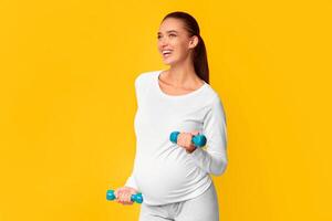 Workout In Pregnancy. Smiling Pregnant Lady Exercising With Dumbbells Standing On Pink Studio Background. Free Space For Text photo