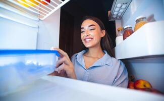 Diet schedule. Cheerful girl taking food container with lunch from fridge, view from inside photo