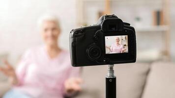 Senior woman is seated on a couch, facing a camera directly in front of her. She appears to be posing or filming a , with a professional setup around her. photo